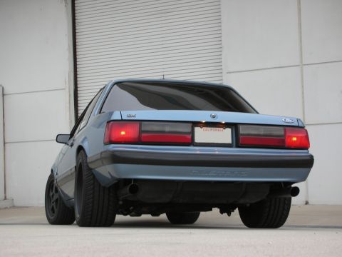 1990 Ford Mustang - Rear view of a blue Ford Mustang with a California license plate and aftermarket exhaust pipes.