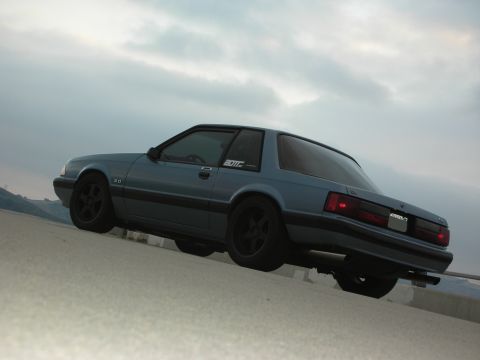 1990 Ford Mustang - A blue 1990 Ford Mustang is parked on a concrete surface under a cloudy sky.