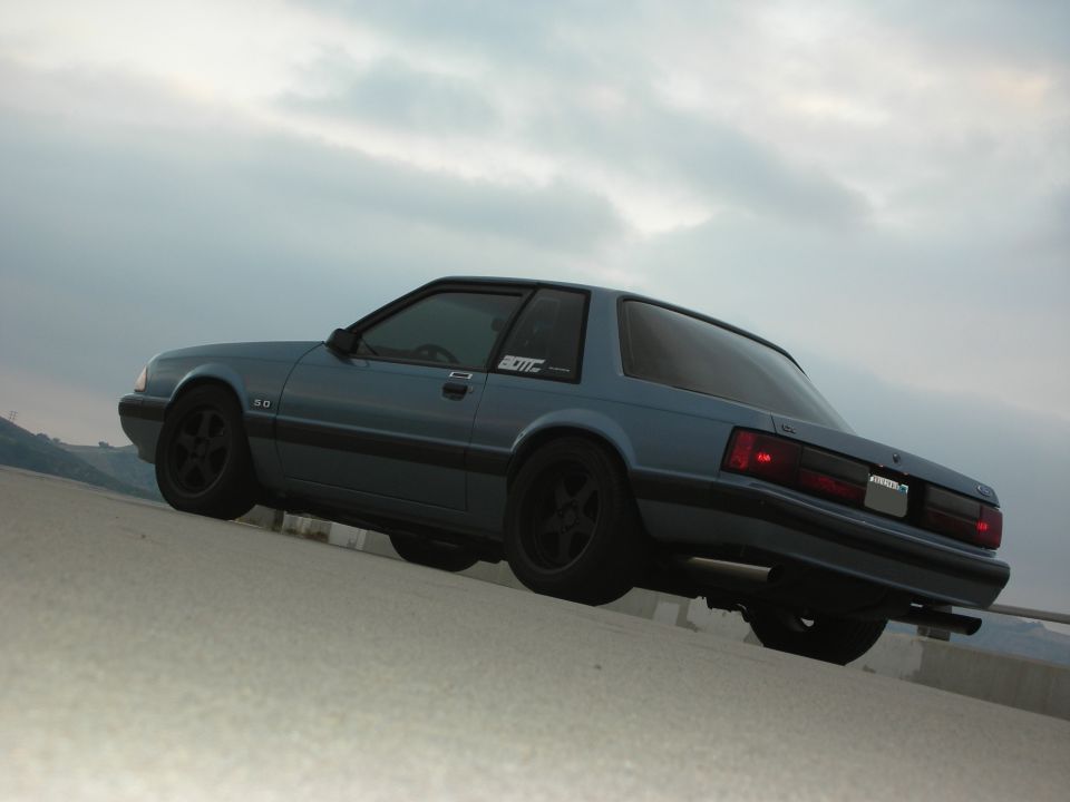 Blue 1990 Ford Mustang coupe, side view, black wheels, cloudy sky