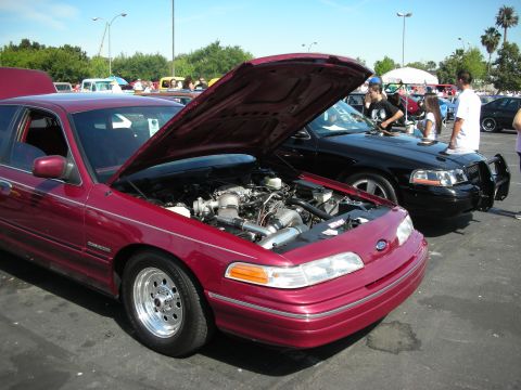 1992 Ford Crown Victoria - A maroon 1992 Ford Crown Victoria is displayed with its hood open, alongside a black police interceptor model.