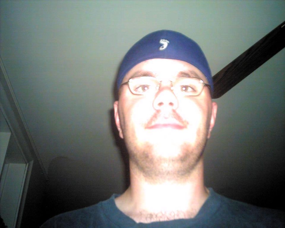 Man in blue beanie and glasses, close-up selfie, with a ceiling fan visible