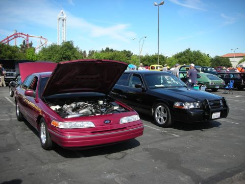 1992 Ford Crown Victoria - Two Ford Crown Victorias are parked at an outdoor car show with a roller coaster in the background.