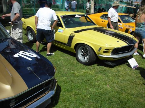 1992 Ford Crown Victoria - A yellow 1970 Ford Mustang Boss 302 is displayed on the grass at an outdoor car show, with other vehicles nearby.