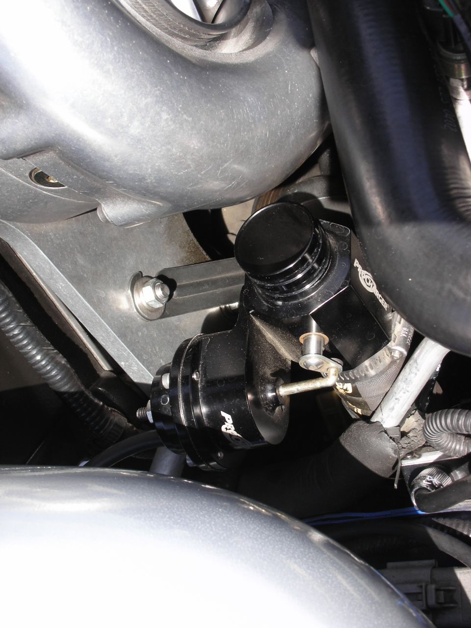 Black blow-off valve assembly with silver lever and black cap, mounted to engine components