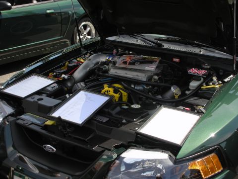 1992 Ford Crown Victoria - The engine bay of a green Ford Mustang is displayed with informational sheets and a second green vehicle is visible behind it.