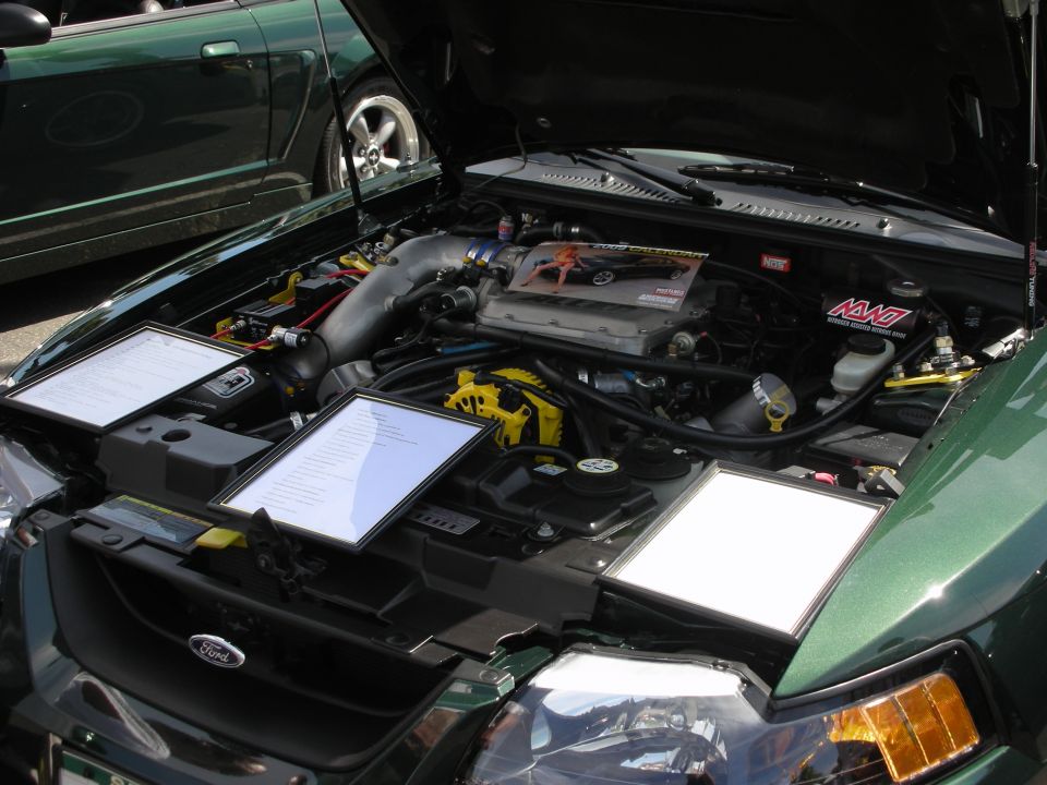 Green Ford Mustang engine bay with informational displays and another green car in the background