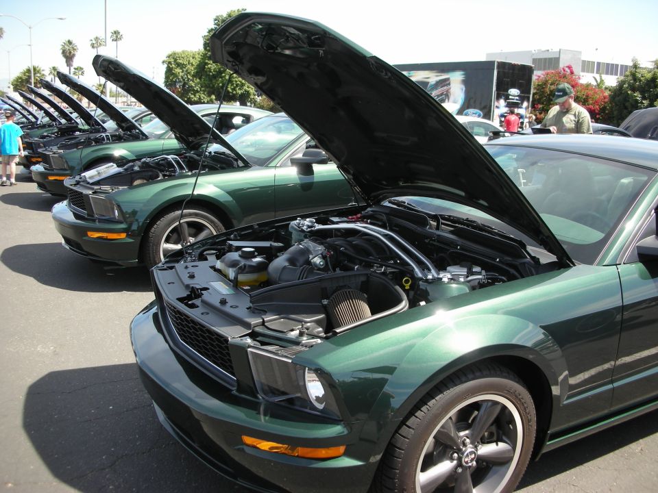 Green Ford Mustang with hoods open, parked in a line