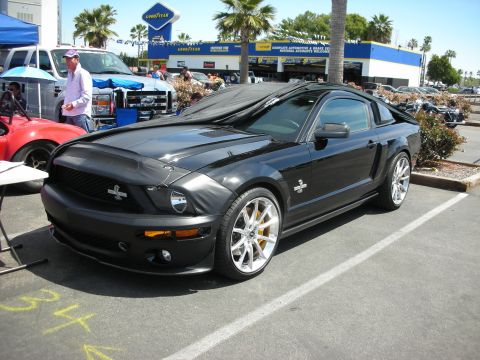 1992 Ford Crown Victoria - A black 2007 Ford Mustang Shelby GT500 is parked at an outdoor event with other vehicles and a Goodyear service center in the background.
