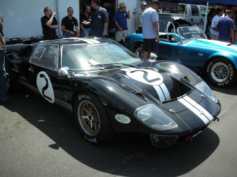 1992 Ford Crown Victoria - A black Ford GT40 race car with white racing stripes and the number 2 is parked next to a blue convertible.