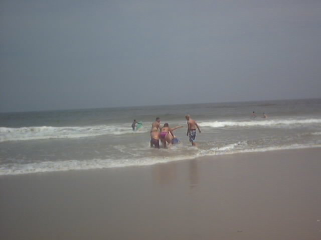 People wading in ocean surf at a beach under an overcast sky