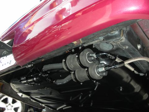 1992 Ford Crown Victoria - Close-up view of the underbody fuel system on a red vehicle, showing dual fuel pumps and associated plumbing.