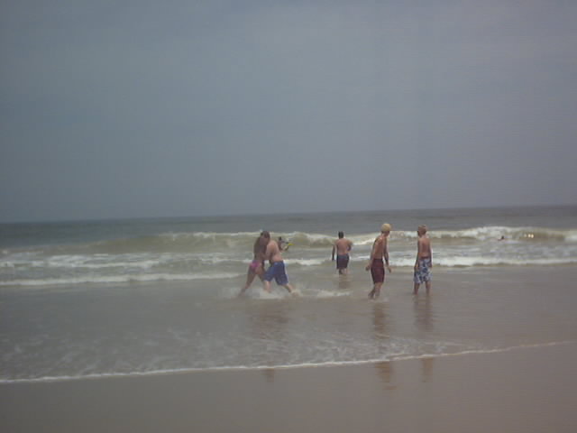 Group of people wading and playing in shallow ocean surf at a gray, overcast beach