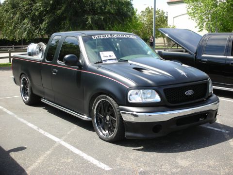 1992 Ford Crown Victoria - This modified black Ford F-150 pickup truck features a matte finish, custom hood, and aftermarket wheels, with a spare tire visible in the…