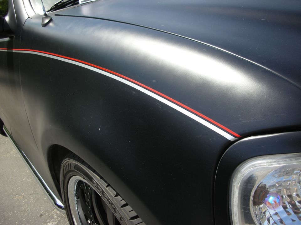 Close-up of a black car's front fender with red and silver pinstripes. Aftermarket wheels are visible