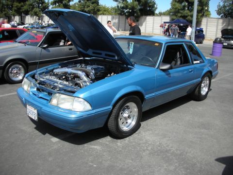 1992 Ford Crown Victoria - Modified blue Ford Mustang coupe at a car show, hood open revealing engine details.