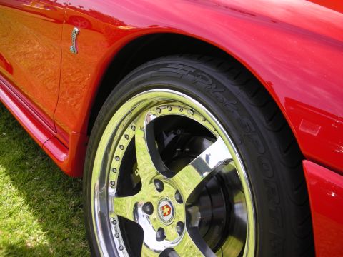 1992 Ford Crown Victoria - A close-up view of a custom chrome wheel and tire on a red sports car, with a cobra emblem visible on the fender.