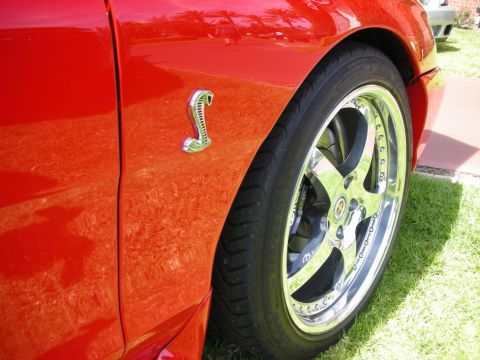 1992 Ford Crown Victoria - Close-up of a red car's fender and wheel, showing a chrome cobra emblem.