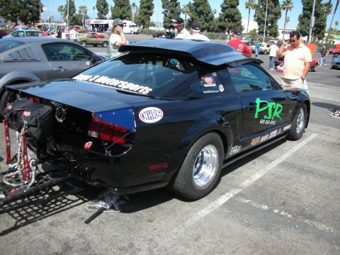 1992 Ford Crown Victoria - A black Ford Mustang modified for drag racing is parked at an outdoor event. Other vehicles and people are visible in the background.