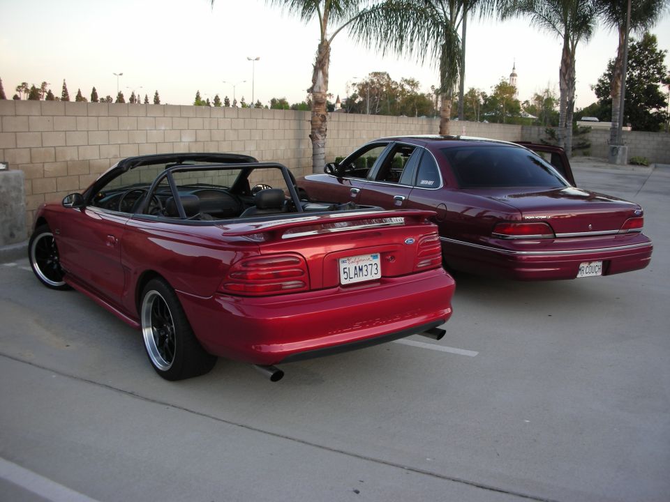 Red SN95 Mustang convertible parked beside a maroon Ford Crown Victoria sedan