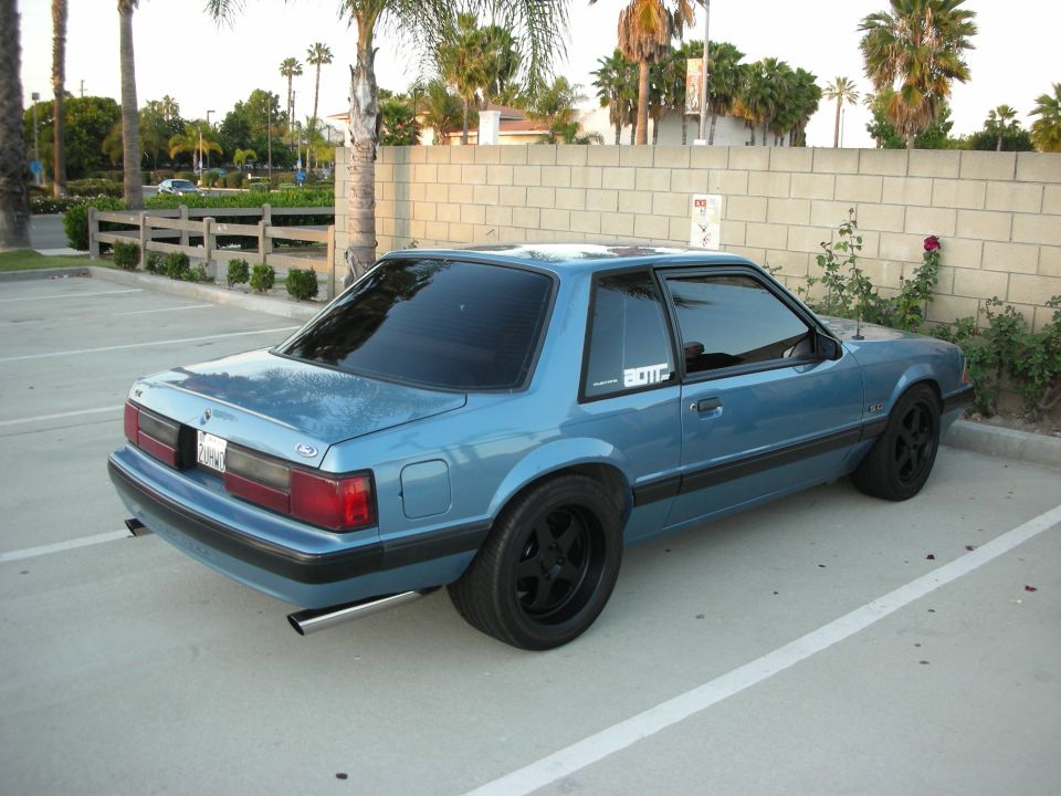 Blue 1987 Ford Mustang coupe with black wheels and exhaust tips parked in a lot