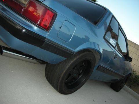 1992 Ford Crown Victoria - A blue coupe with a custom exhaust and black wheels is parked on a paved surface.