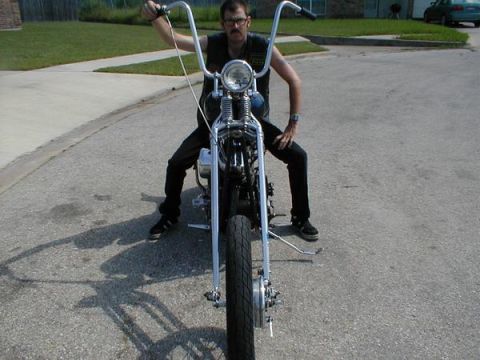 1948 Harley-Davidson FL - A man sits astride a custom motorcycle, its front end and high handlebars prominently displayed in this street-level shot.