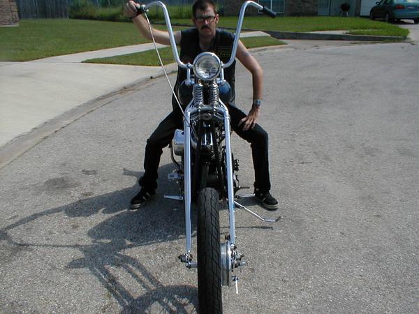 Front view of a custom motorcycle with high handlebars and a rider