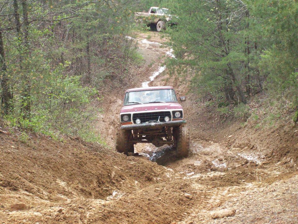 Maroon and white Ford Bronco climbing a rutted clay trail with front axle exposed