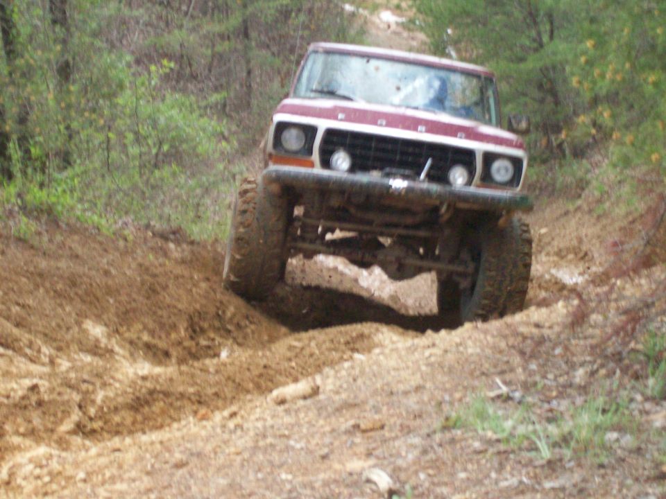 Maroon and white 1970s Ford Bronco flexing on a rutted dirt trail with solid front axle exposed
