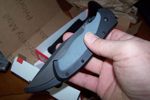 1990 Ford Bronco - A person holds a folding knife with a gray textured grip and black blade, with a shipping box visible behind it.