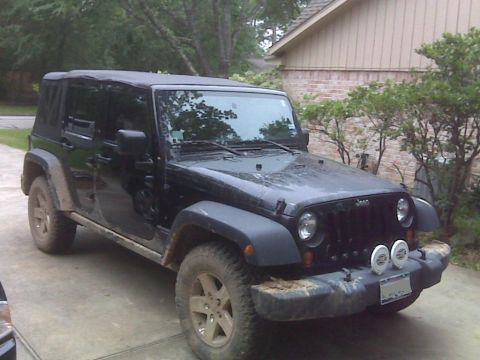 2008 Jeep Wrangler - Black Jeep Wrangler with soft top parked on a driveway, showing its front 3/4 view.