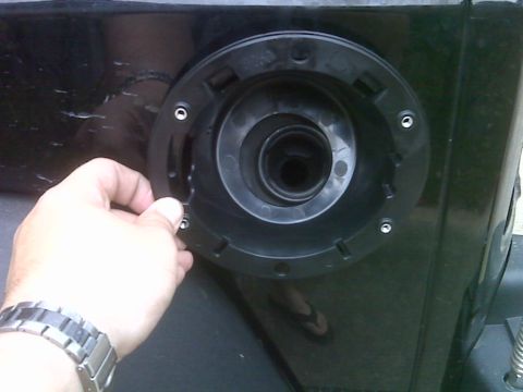 2008 Jeep Wrangler - Close-up of a fuel filler neck assembly being held in place, with a website logo in the corner.