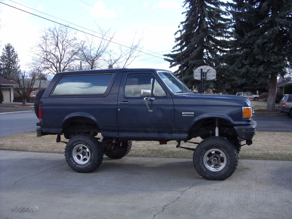 Faded dark blue lifted Ford Bronco XLT side view on a suburban driveway