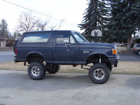 1988 Ford Bronco - A dark blue Ford Bronco is parked on a concrete driveway, modified with a lift kit and large tires.