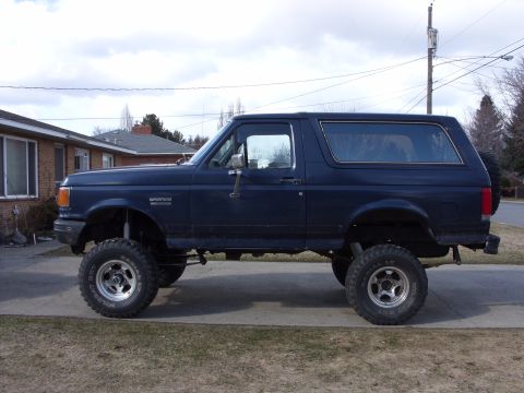 1988 Ford Bronco - A lifted 1988 Ford Bronco is shown from the side, parked in front of a residential house.