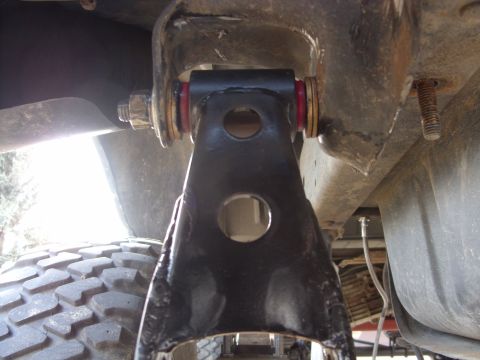 1988 Ford Bronco - Undercarriage view of a vehicle's suspension system, a black arm with red bushings and a portion of a tire.