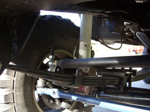 1988 Ford Bronco - Underbody view of a lifted 4x4 front suspension showing multi-leaf springs, a black sway bar with an end link, tie rod and drag link, and a…