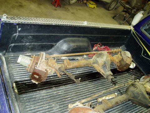 2000 Ford E350 - Two rusty rear axles are loaded into the bed of a pickup truck, along with other vehicle parts.