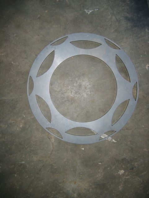 1992 Ford Mustang - A circular metal part with decorative oval cutouts, likely a wheel cover, lies on a concrete surface.