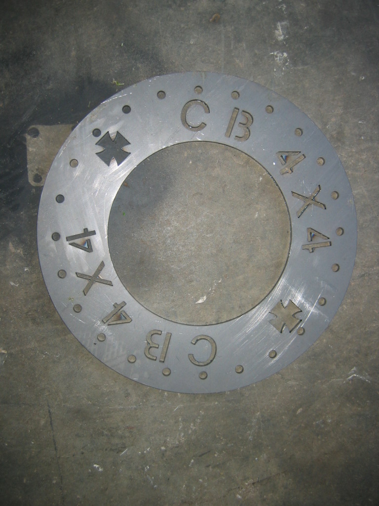 Gray metal disc with holes around the edge and 'CB', '4X4', and cross symbols cut out