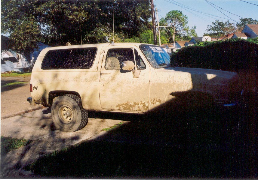 Mud-covered square-body two-door 4x4 SUV parked in a driveway, passenger side