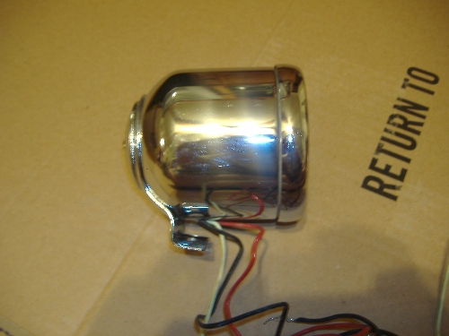 Chrome headlight assembly with red, black, and white wires. Cardboard box with 'RETURN TO' text visible