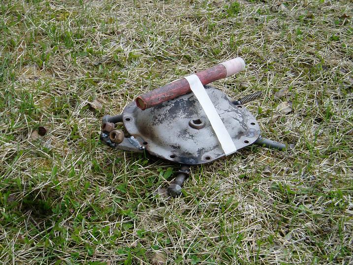 Differential cover with a pipe taped to it, lying on grass