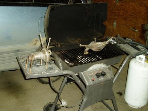 2000 Ford E350 - A propane grill with two metal sculptures on it sits in front of a light blue vehicle. A white propane tank is to the right of the grill.
