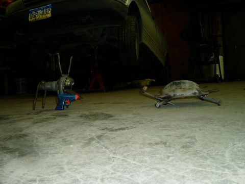 2000 Ford E350 - A metal sculpture resembling a turtle and another resembling an insect with a toy gun are on a concrete floor in front of a vehicle.