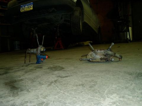 2000 Ford E350 - Two scrap metal sculptures resembling robots are on a concrete floor in a garage. A car is raised on jack stands in the background.