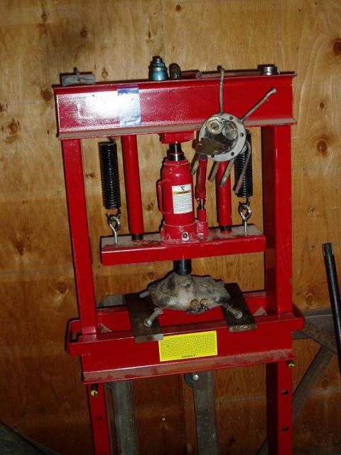 2000 Ford E350 - A red hydraulic press is set up with a car part, possibly a differential or transmission component, being worked on at the bottom. A hydrau…