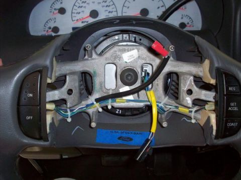 2007 Ford Mustang - Interior view of a steering wheel with exposed wiring and a blue Ford label.