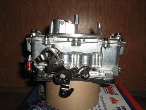1988 Mercury Grand Marquis - A close-up view of a carburetor, a critical engine component, is presented against a wood-grain background.