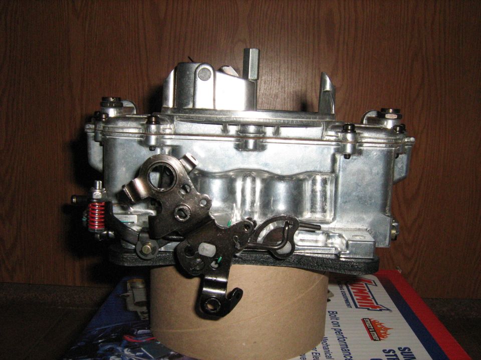 Chrome carburetor with linkage and red spring, resting on a cardboard tube